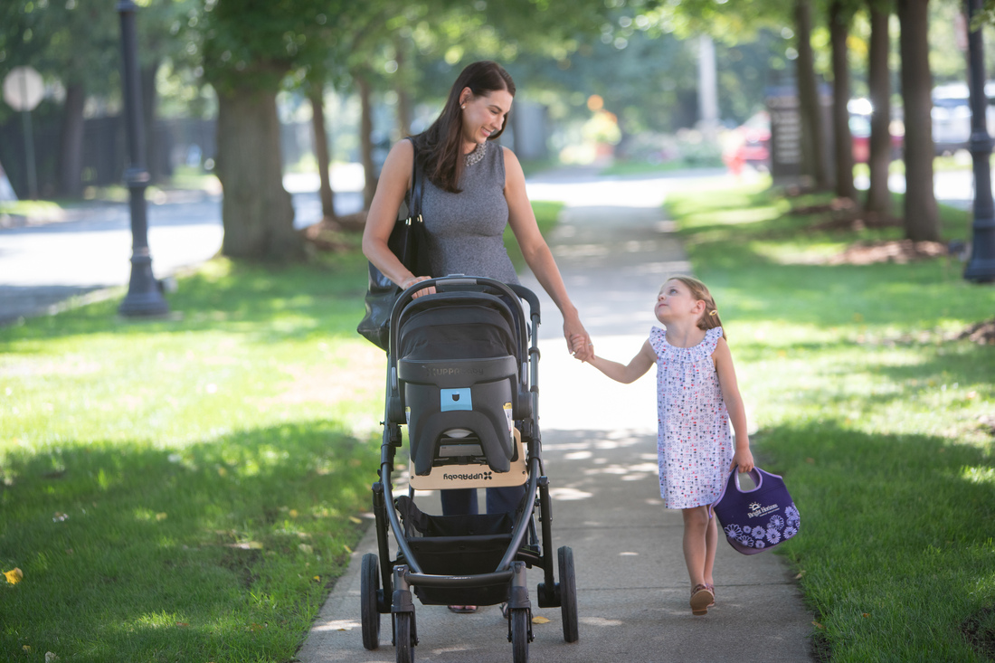 Mother and daughter walking in park with stroller and backpack on sunny day.