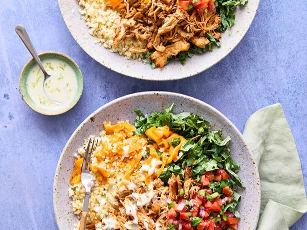 Fresh salads with shredded chicken, cheese, and vegetables on a blue table.